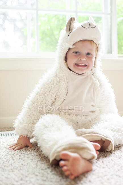 Portrait of happy young boy in llama costume sitting on floor at home — Stock Photo