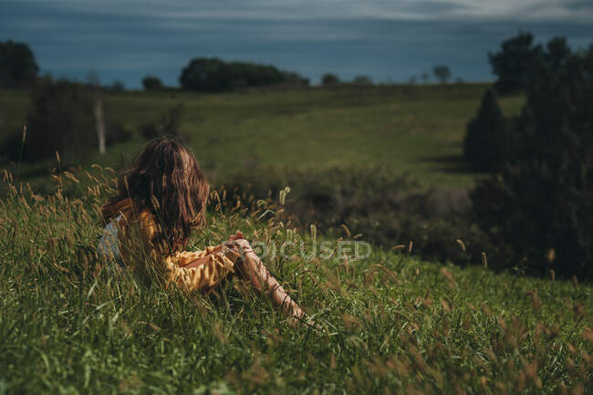 Tween chica mirando lejos en una ladera verde con cielos oscuros - foto de stock