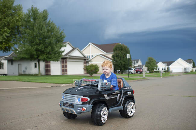 Jeune garçon conduit voiture jouet électrique dans la rue du quartier — Photo de stock