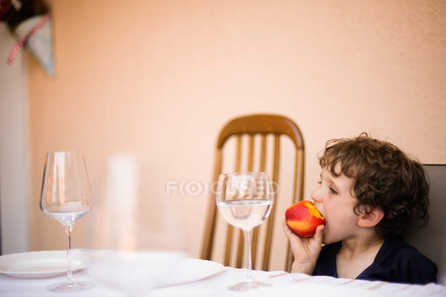 A young boy eating a peach outside during the summer — Stock Photo