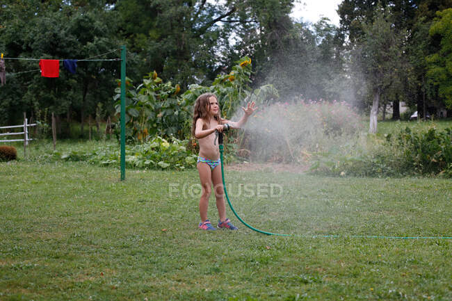 Uma menina brincando com a mangueira em um dia quente de verão — Fotografia de Stock