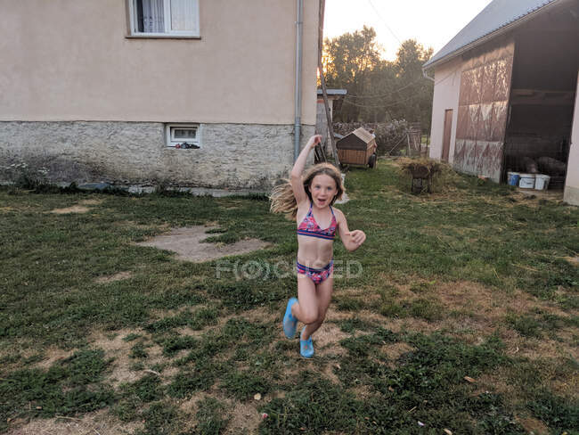 Счастливая девушка, бегущая через двор на ферме — стоковое фото