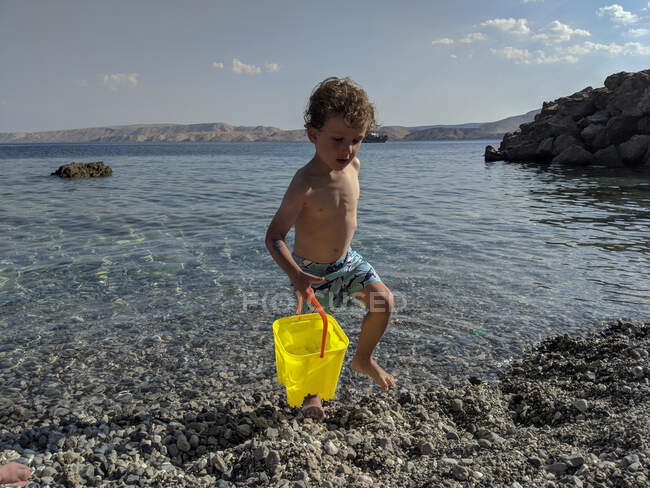 Menino carregando um amarelo pálido brilhante de água perto do mar — Fotografia de Stock