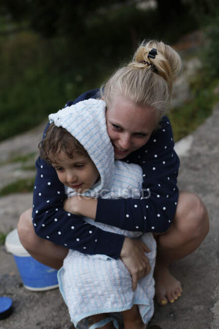 Eine junge erwachsene Frau umarmt einen kleinen Jungen nach dem Schwimmen — Stockfoto