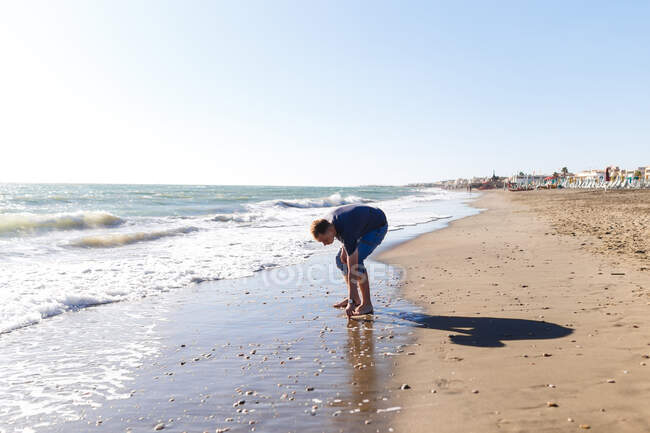 Rubio chico turista en jeans disfrutando de la playa y el mar - foto de stock