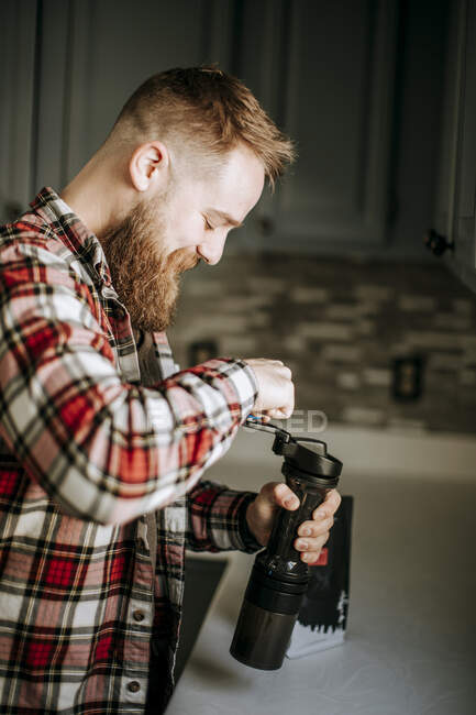 Homem com sorrisos de barba ao moer café em sua cozinha de manhã — Fotografia de Stock