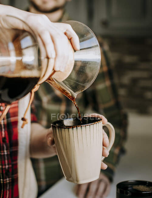 Heißer Kaffee wird aus einer Gießkanne in eine braune Kaffeetasse gegossen — Stockfoto