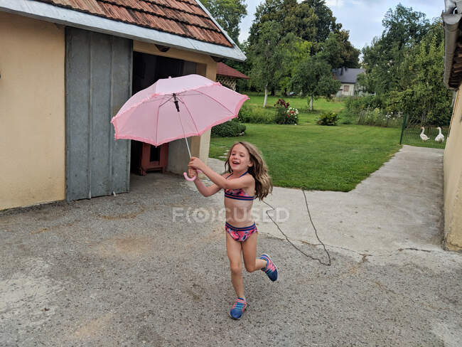 Маленькая девочка бегает с зонтиком во время летнего дождя — стоковое фото