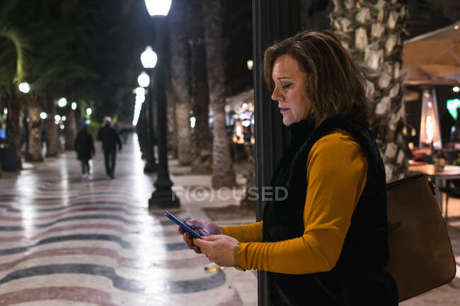 Женщина средних лет смотрит на свой смартфон на улице — стоковое фото