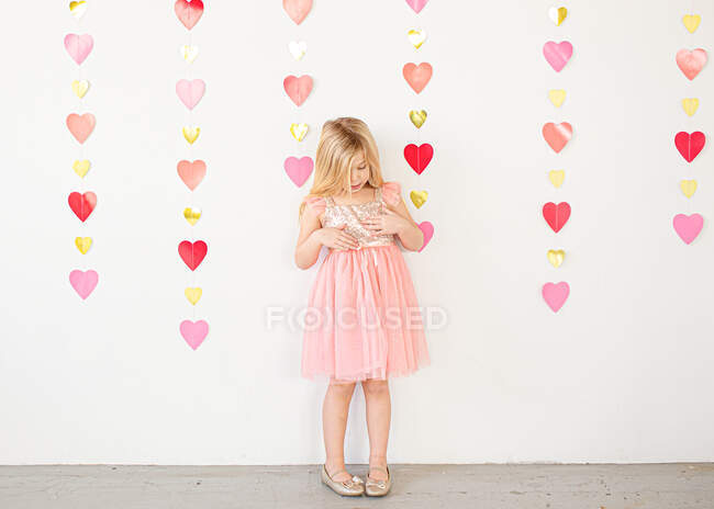 Young blond girl in fancy dress in front of hearts indoors — Stock Photo