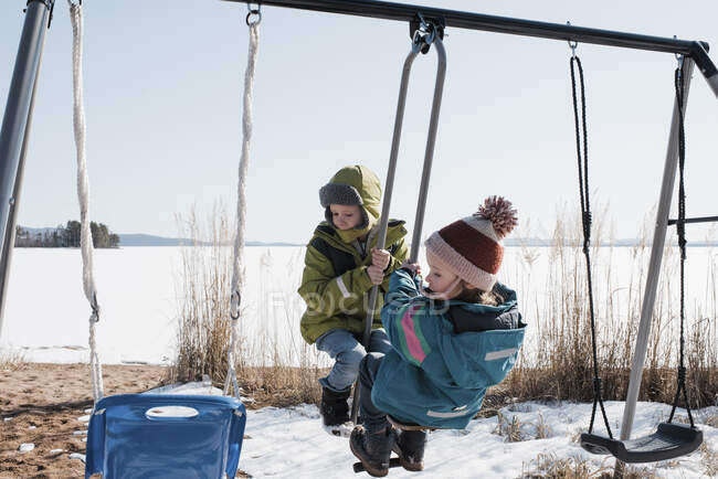 Enfants jouant sur une double balançoire ensemble au bord du lac en Suède — Photo de stock