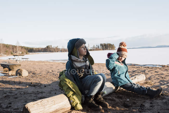 Crianças sentadas em um tronco perto de um lago congelado na Suécia — Fotografia de Stock