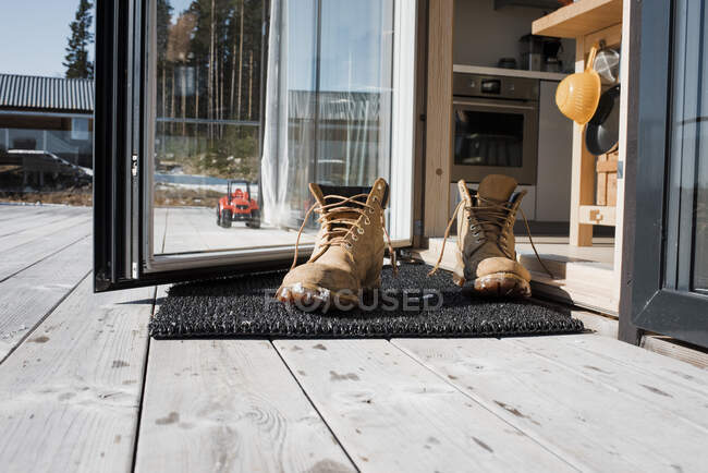 Botas masculinas em um tapete na porta das traseiras em uma varanda em casa — Fotografia de Stock