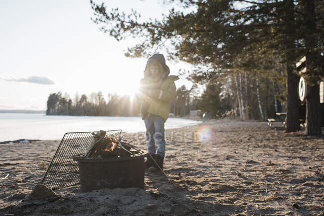 Young boy stood next to a fire on the beach in Sweden — Stock Photo
