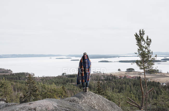 Frau in eine Decke gehüllt mit Blick auf das Meer und den Wald — Stockfoto
