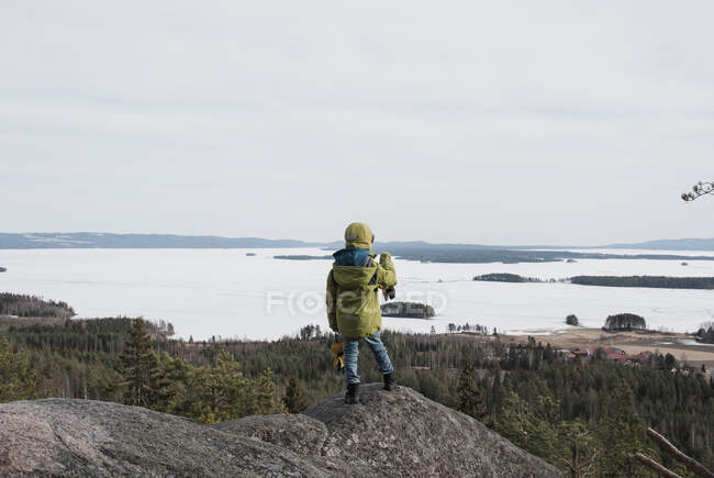 Мальчик, стоящий на скале и смотрящий на океан — стоковое фото
