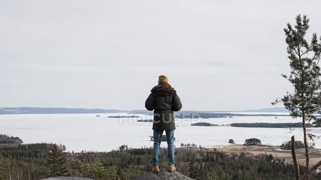 Hombre de pie sobre una roca alta disfrutando de la hermosa vista al mar - foto de stock