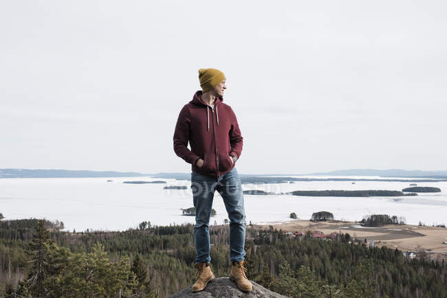 Hombre de pie sobre una roca mientras camina una colina sobre el océano en Suecia - foto de stock