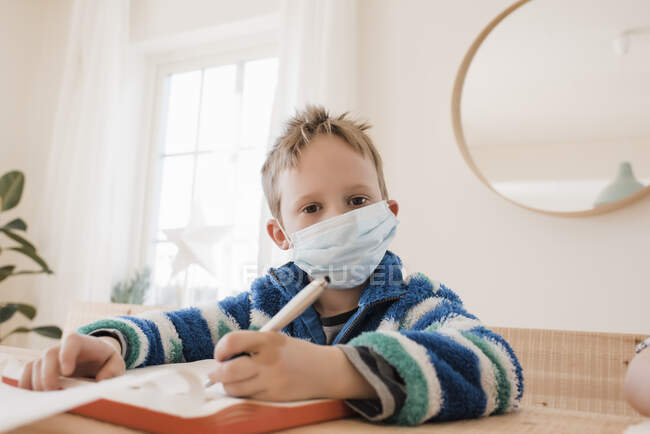 Educación en el hogar de un niño con una máscara médica para protegerse de un virus - foto de stock