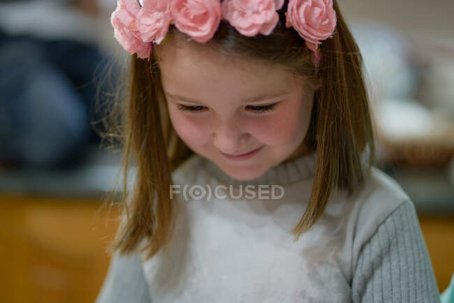 Menina com uma cabeça de flor vermelha olha para baixo sorrindo — Fotografia de Stock