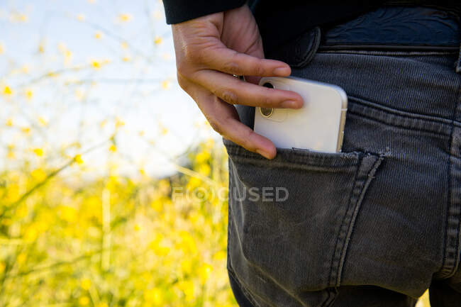 Жінка витягує мобільний телефон з кишені штанів в природі — стокове фото