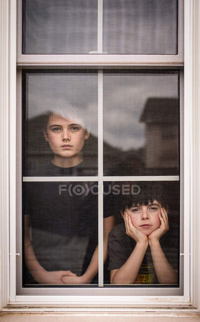 Deux garçons regardant par la fenêtre avec des visages ennuyés — Photo de stock