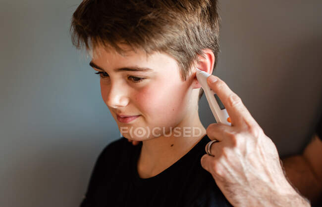 Tween boy getting temperature taken with an ear thermometer. — Stock Photo