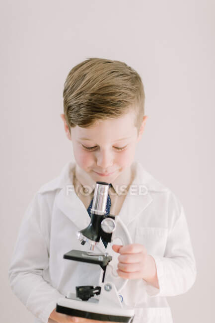 Niño pequeño en gabardina mirando al microscopio - foto de stock
