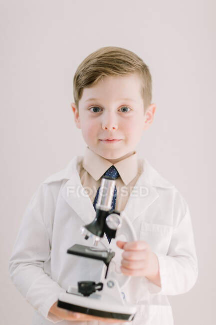 Niño pequeño sosteniendo un microscopio sonriendo a la cámara - foto de stock