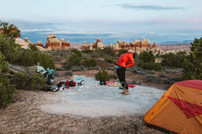 Female camper in orange puffy jacket takes a swig of whiskey in desert — Stock Photo