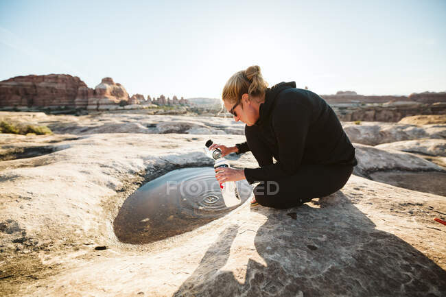Woman in all black scoops drinking water from a puddle in the desert — Stock Photo