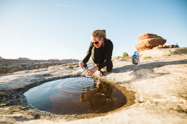 Excursionista recoge agua potable de un charco poco profundo en el desierto - foto de stock