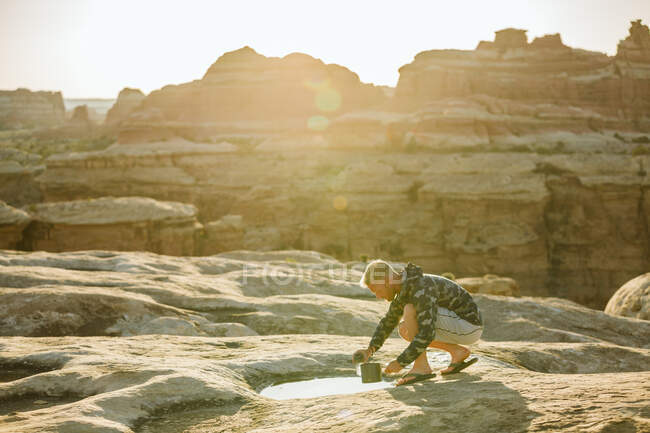 Blonde man in camouflage jacket collects water from a puddle in desert — Stock Photo