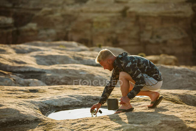 Man in camo jacket collects cooking water from a shallow puddle — Stock Photo