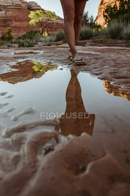 Reflet dans la flaque d'eau des jambes de la femme marchant dans des tongs dans le désert mu — Photo de stock