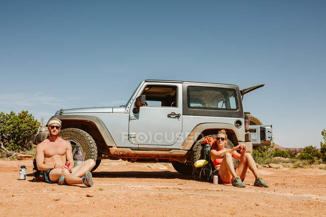Dos excursionistas sentados frente a un jeep - foto de stock