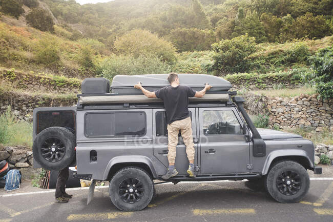 Vue latérale de l'homme merveilleux chargeant des choses sur la jeep à la campagne — Photo de stock