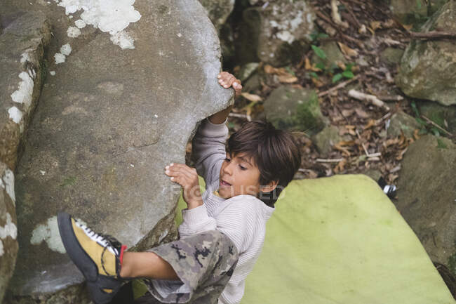 Un niño pequeño trepa una roca al aire libre - foto de stock