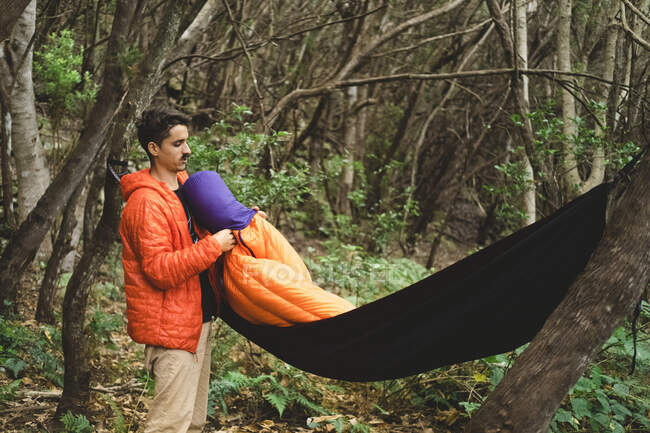 Мужчина собирает спальный мешок и гамак в кемпинге в лесу — стоковое фото