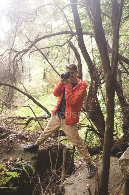 Un joven toma una foto en un bosque lluvioso - foto de stock