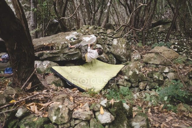 Un niño trepa una roca en un bosque - foto de stock