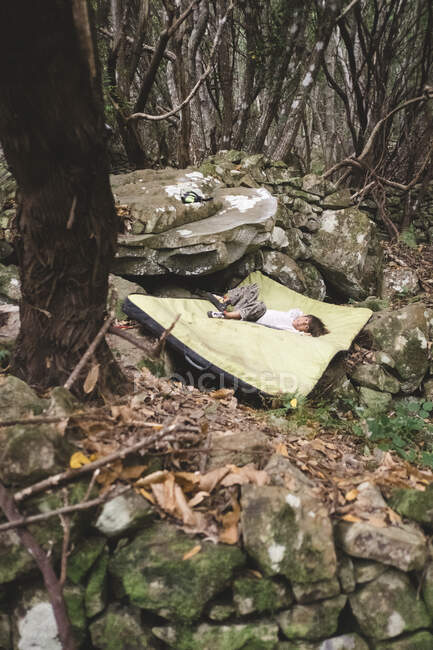 Un jeune enfant se repose après avoir escaladé un rocher dans une forêt — Photo de stock