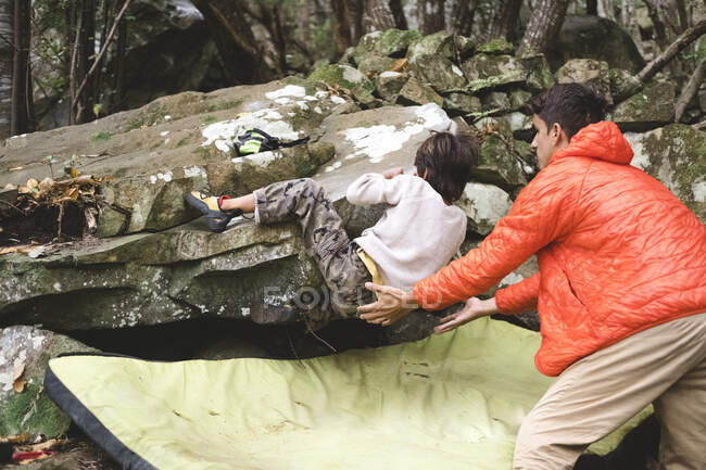 Un jeune enfant grimpe un rocher et son père s'occupe de lui. — Photo de stock