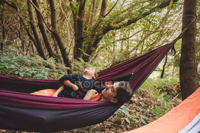 A man and a young kid lying in a hammock in the forest — Stock Photo