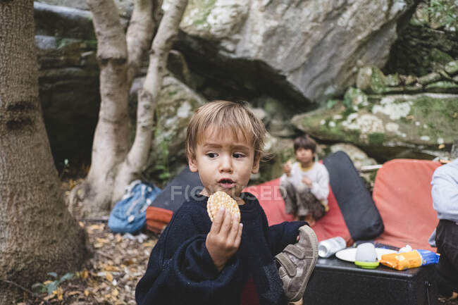 Porträt eines kleinen Kindes, das auf einem Zeltplatz im Wald einen Keks isst — Stockfoto