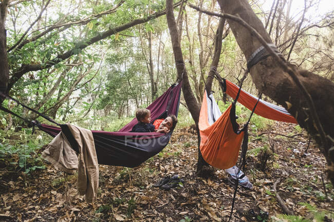 A man and young kid lying in a hammock in the forest — Stock Photo