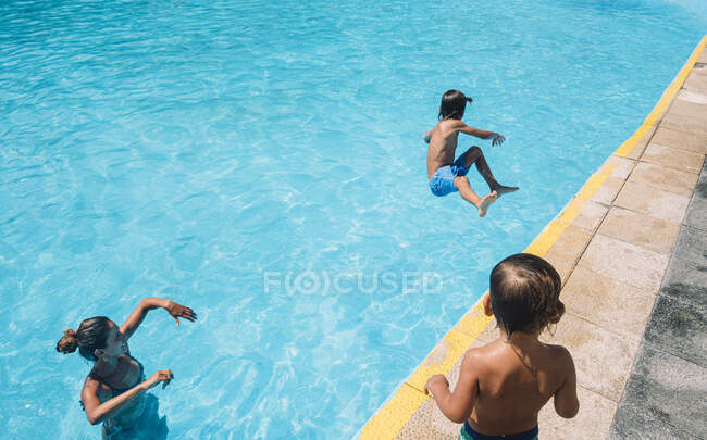 Uma mulher e uma criança olham para um rapaz a saltar para uma piscina. — Fotografia de Stock