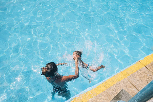 Женщина помогает своему ребенку прыгнуть в бассейн — стоковое фото