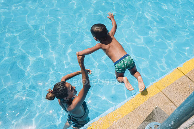 Жінка допомагає дитині стрибати в басейн — стокове фото