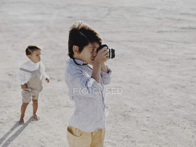 Kid prend des photos avec un appareil photo vintage pendant que l'autre enfant se tient en arrière-plan — Photo de stock